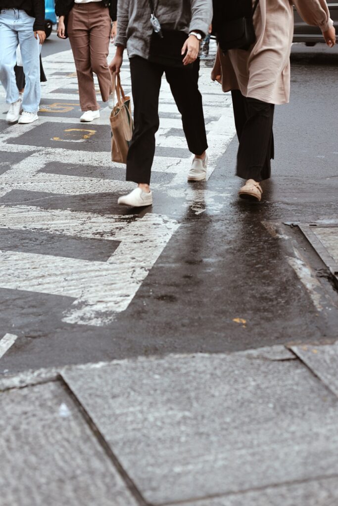 Pedestrians crossing a wet city street at a marked crosswalk in St. Louis.